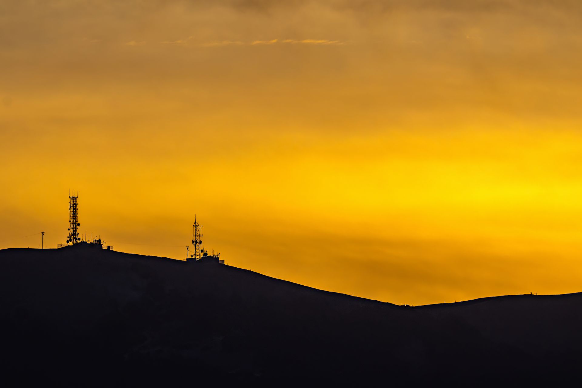 Stunning silhouette of communication towers on a hill against a vibrant sunset sky.