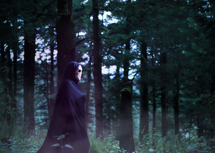 A Person In A Mask And A Robe Walking In A Forest