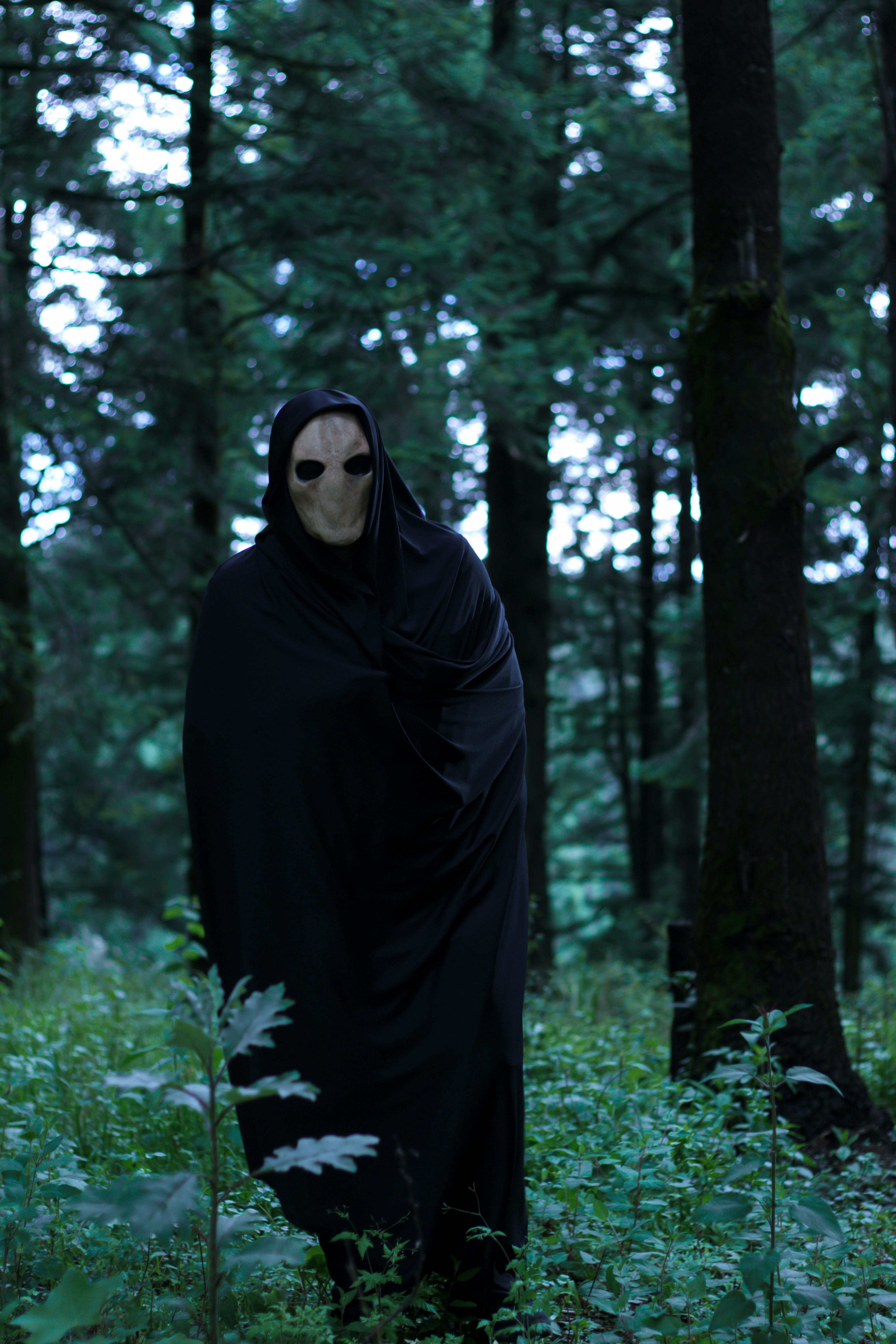 creepy guy in mask wearing black robe in the woods