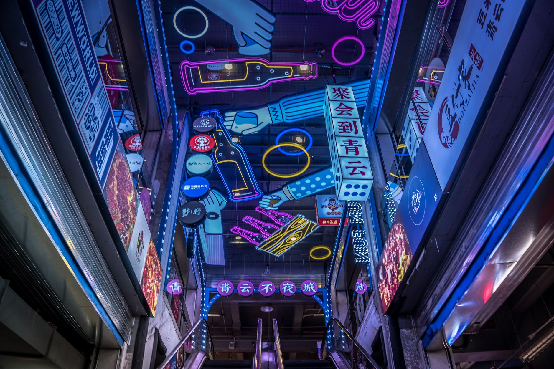 Colorful neon signs in a vibrant indoor setting with escalators and Chinese characters.