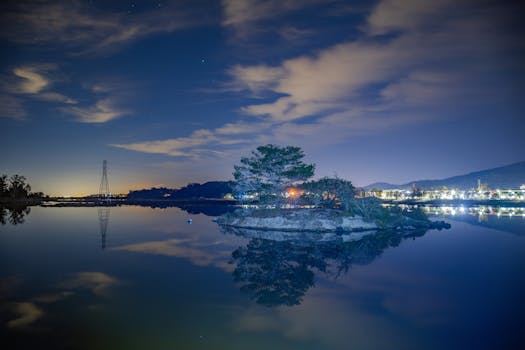 Peaceful night scene of island and reflections on a tranquil lake near city lights.