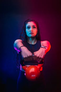 Portrait of a woman lifting a kettlebell in dramatic lighting, showcasing strength and fitness.