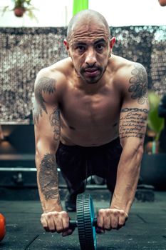 Man with tattoos using an ab wheel for workout, showcasing muscular physique.
