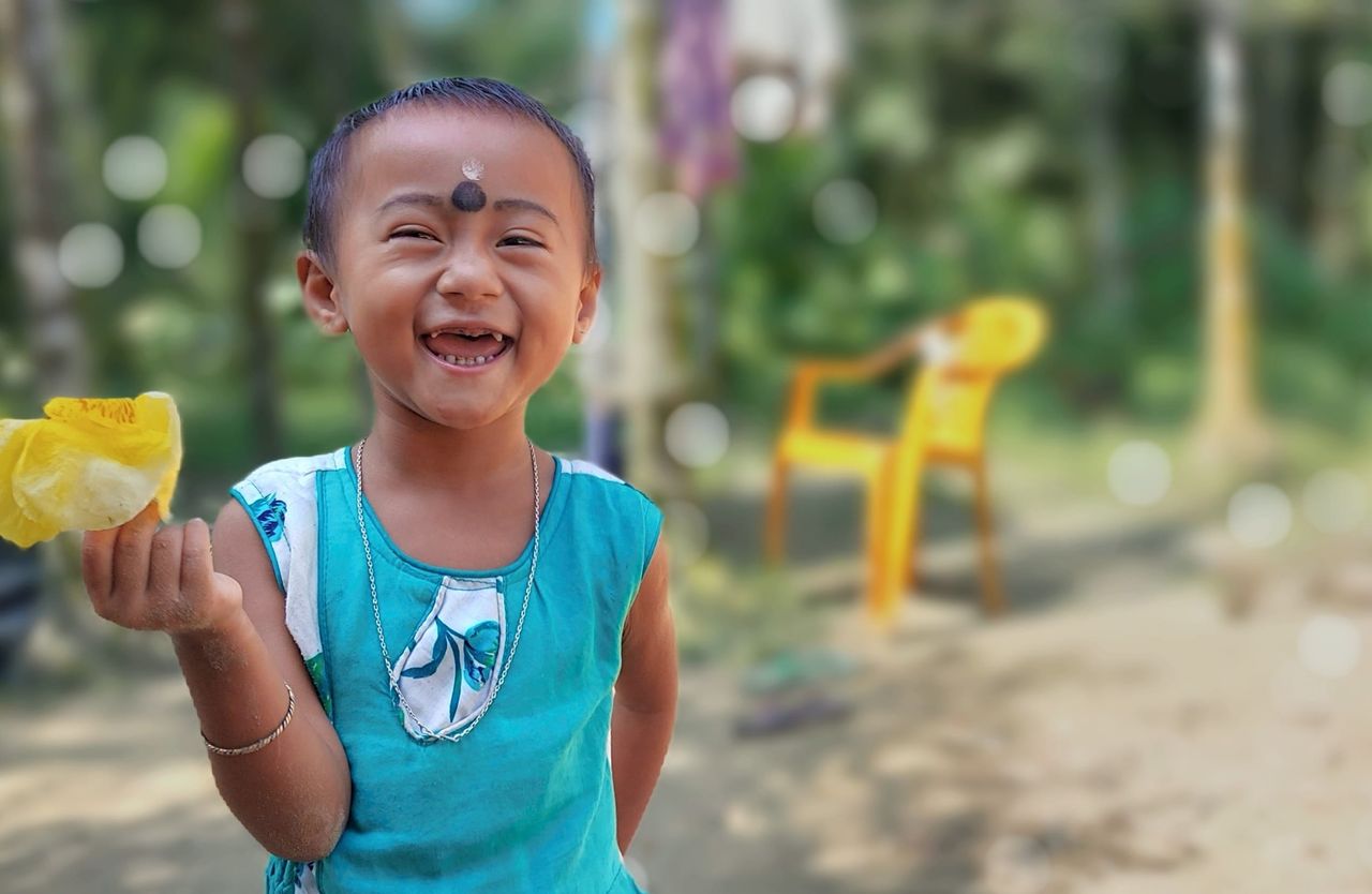 cheerful child in a blue outfit laughing with a fruit in hand enjoying