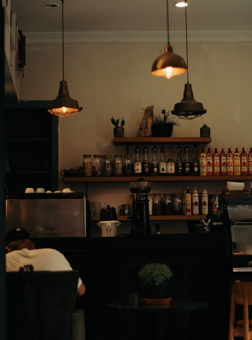 Free Warm and inviting café interior featuring a bar counter with shelves and soft lighting, ideal for dining or coffee breaks. Stock Photo