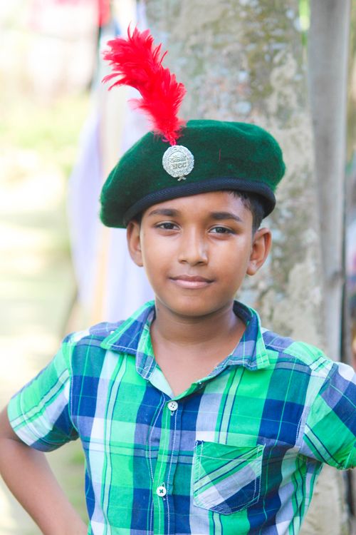 Free A young boy poses outdoors wearing a green hat with a red feather, embodying a vibrant and playful spirit. Stock Photo