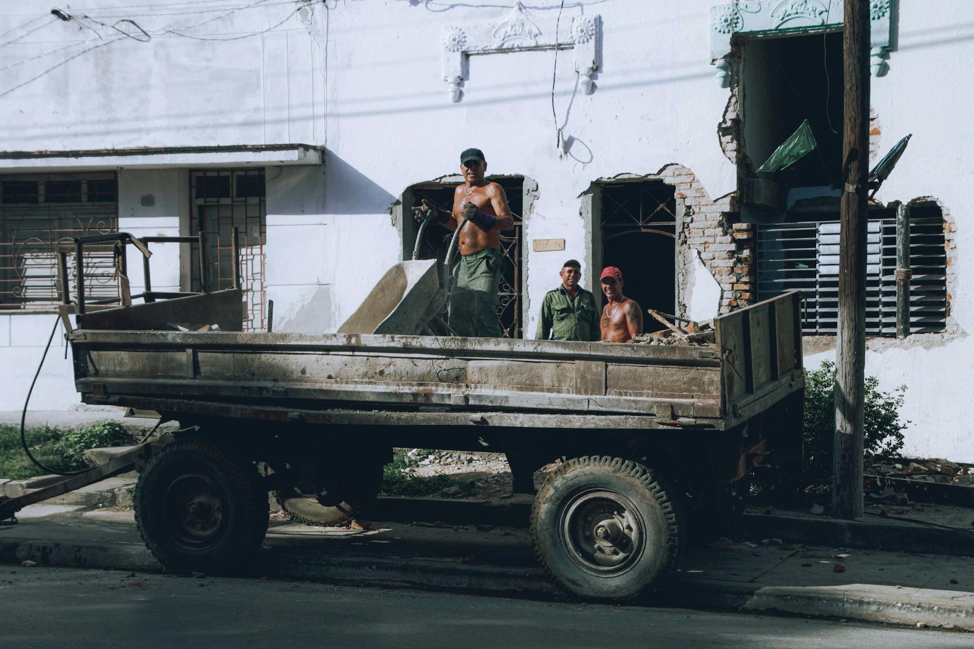 Workers loading debris onto a truck at an urban construction site. Manual labor in progress.