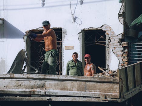 Three construction workers renovating building exterior on a sunny day.