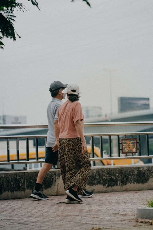 Free A man and a woman walk together outdoors with face masks near a metal railing. Stock Photo