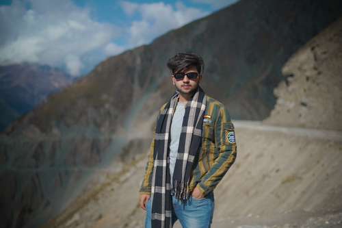 Free Casual young man wearing sunglasses and scarf posing confidently in a scenic mountain landscape. Stock Photo