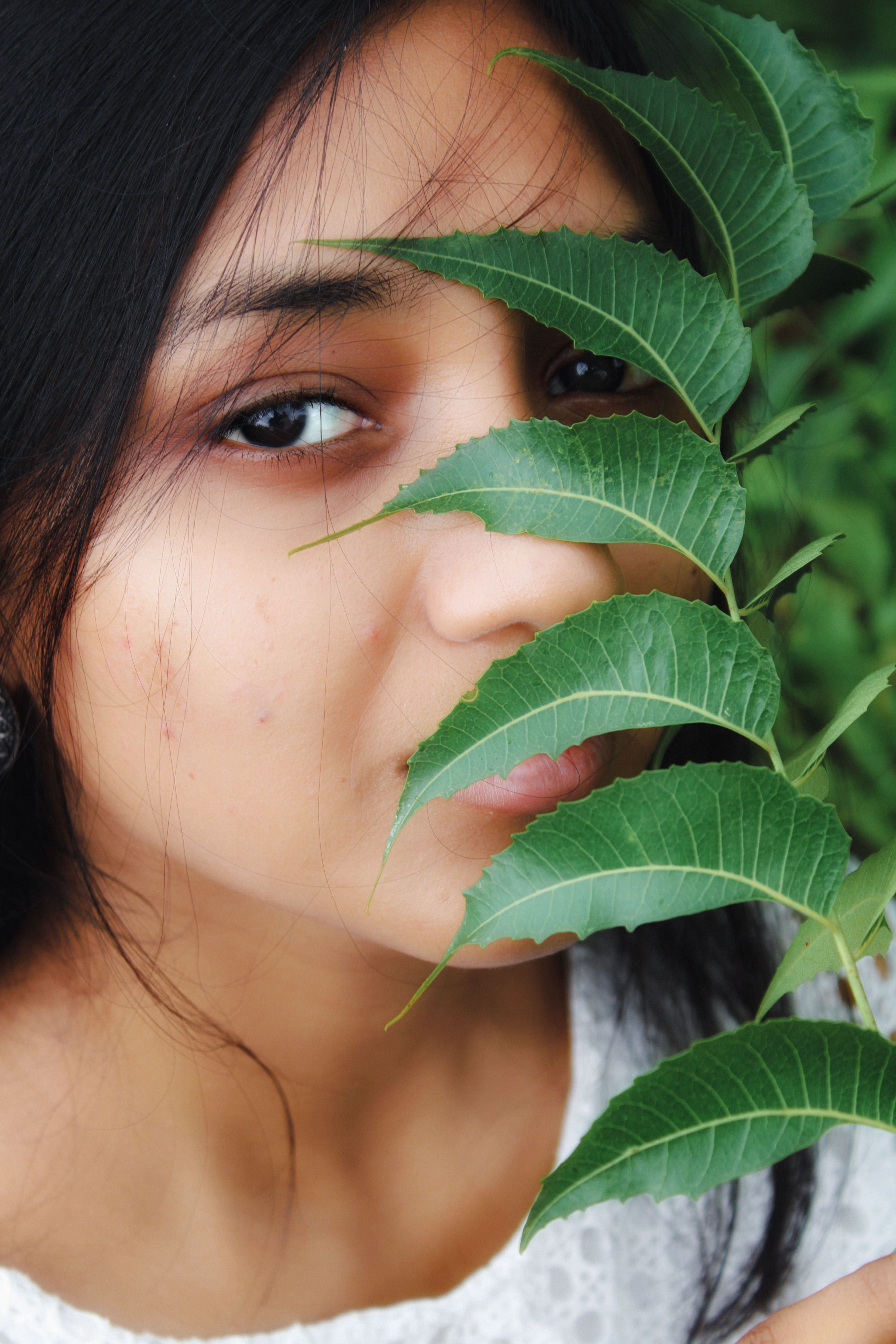 Close-up of a woman partially hidden by green foliage, conveying mystery.