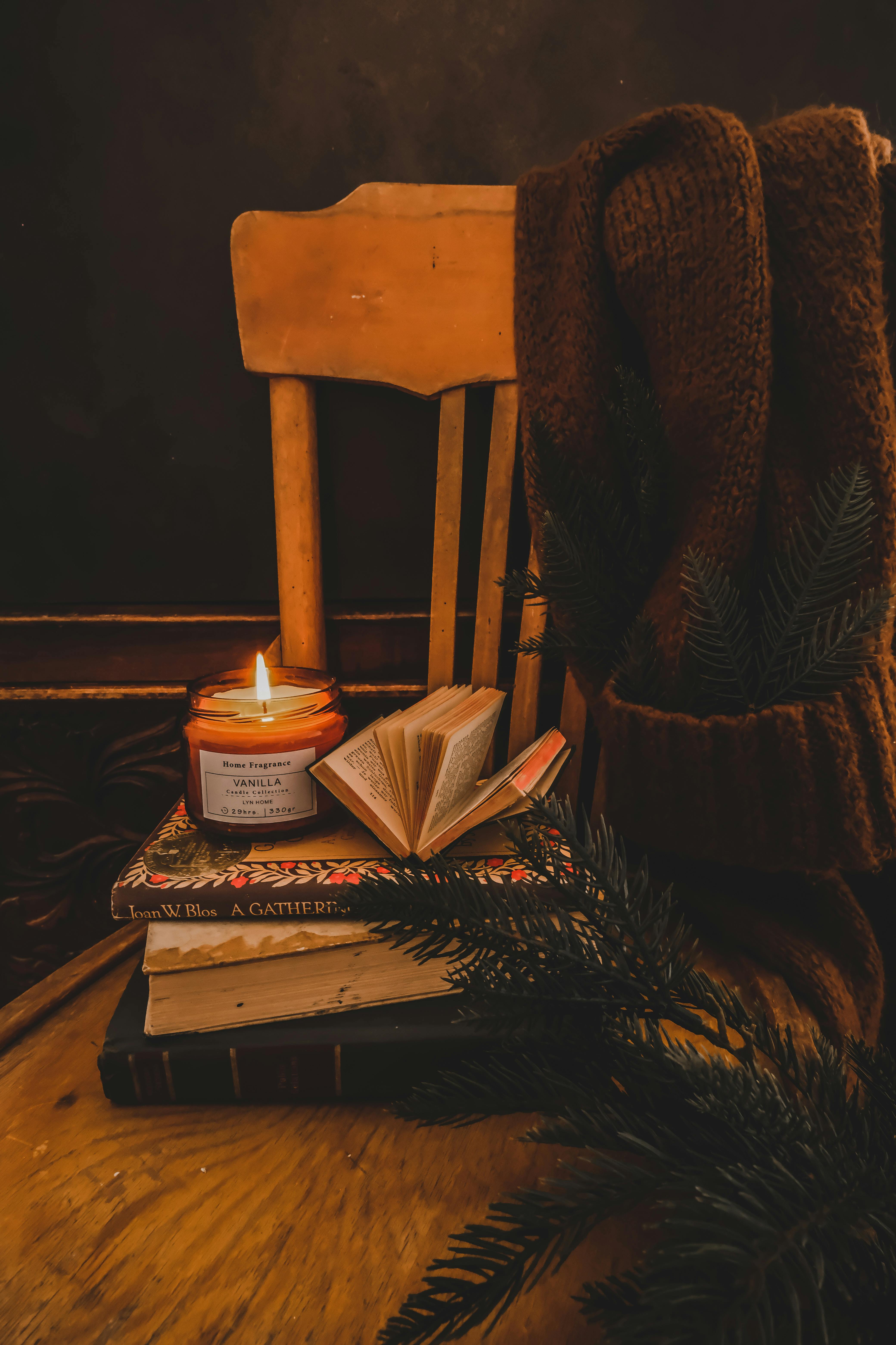 Free Warm and inviting reading nook with books, a lit candle, and a cozy sweater on a chair. Stock Photo
