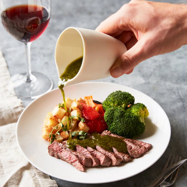 A Close-Up Shot Of A Person Pouring Sauce On A Steak Meal