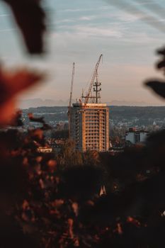 Urban high-rise building construction with cranes amidst a scenic backdrop at dusk.