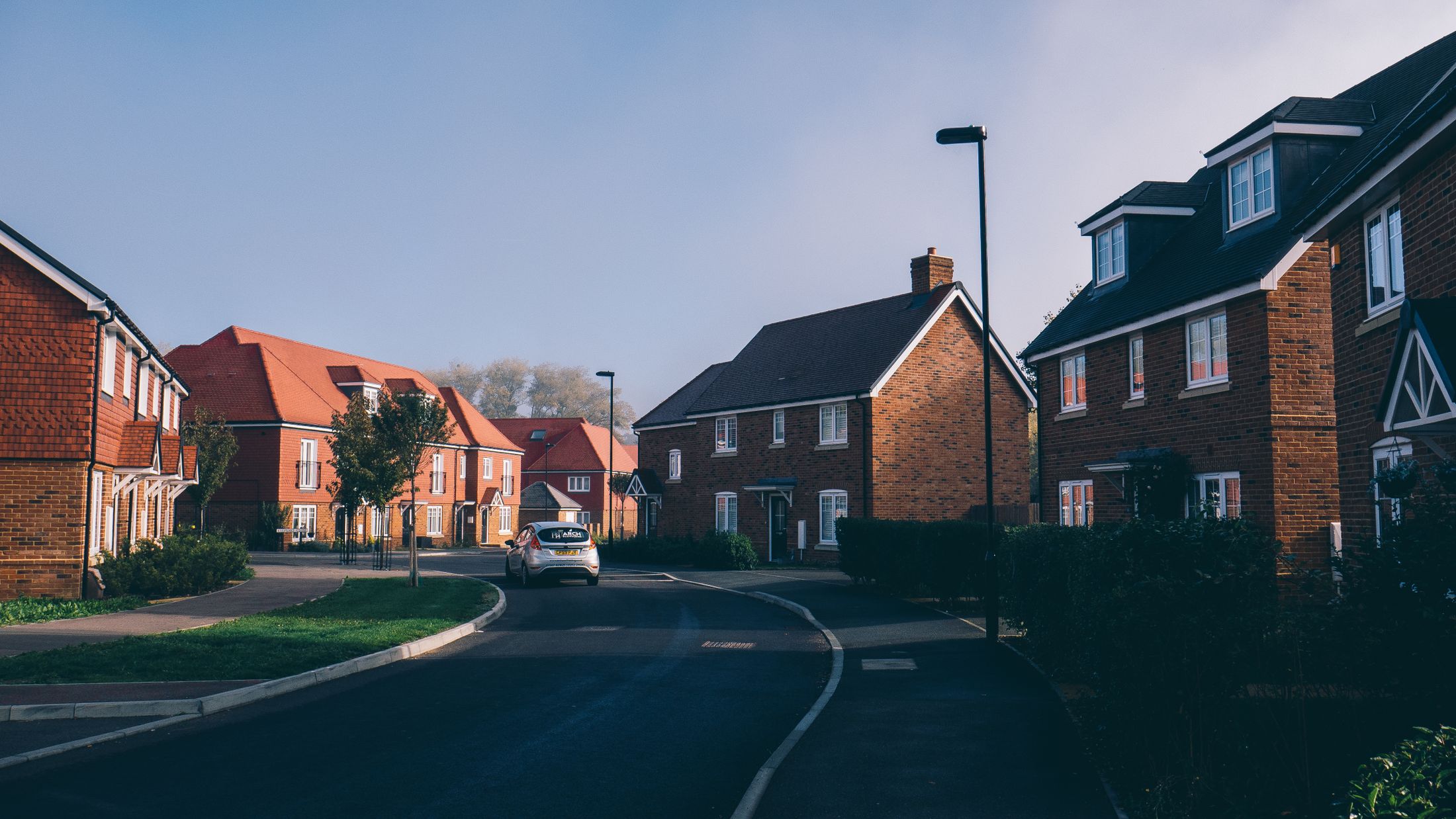 A quiet English suburban street lined with red-brick houses at first light