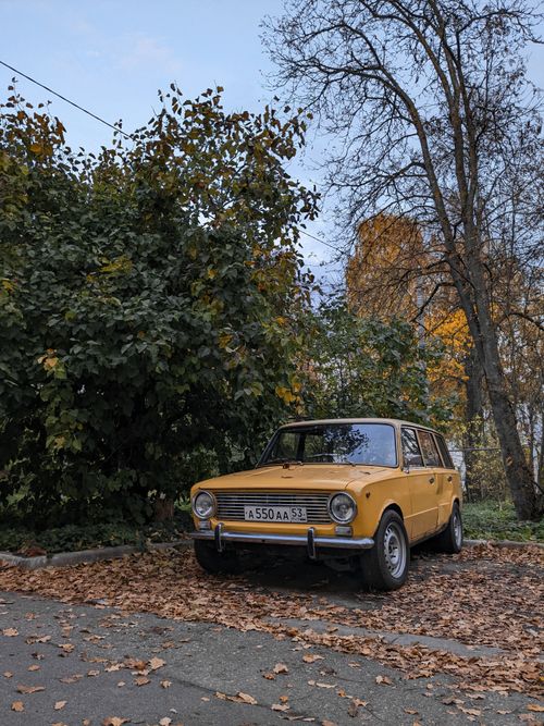 Free A classic yellow car parked among fallen leaves in an autumn landscape, evoking nostalgia. Stock Photo