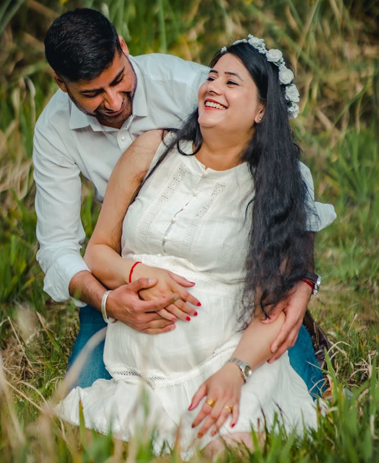 Smiling Man In Shirt And Pregnant Woman In White Shirt Kneeling On Grass