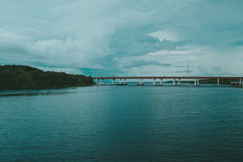 Free Serene view of a red bridge spanning over the tranquil ocean under a cloudy sky. Stock Photo