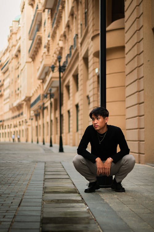 Man Squatting on Sidewalk