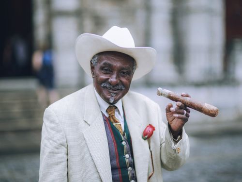 Free Smiling elderly man in cowboy hat, holding a cigar, portraying elegance and joy in a classic portrait. Stock Photo