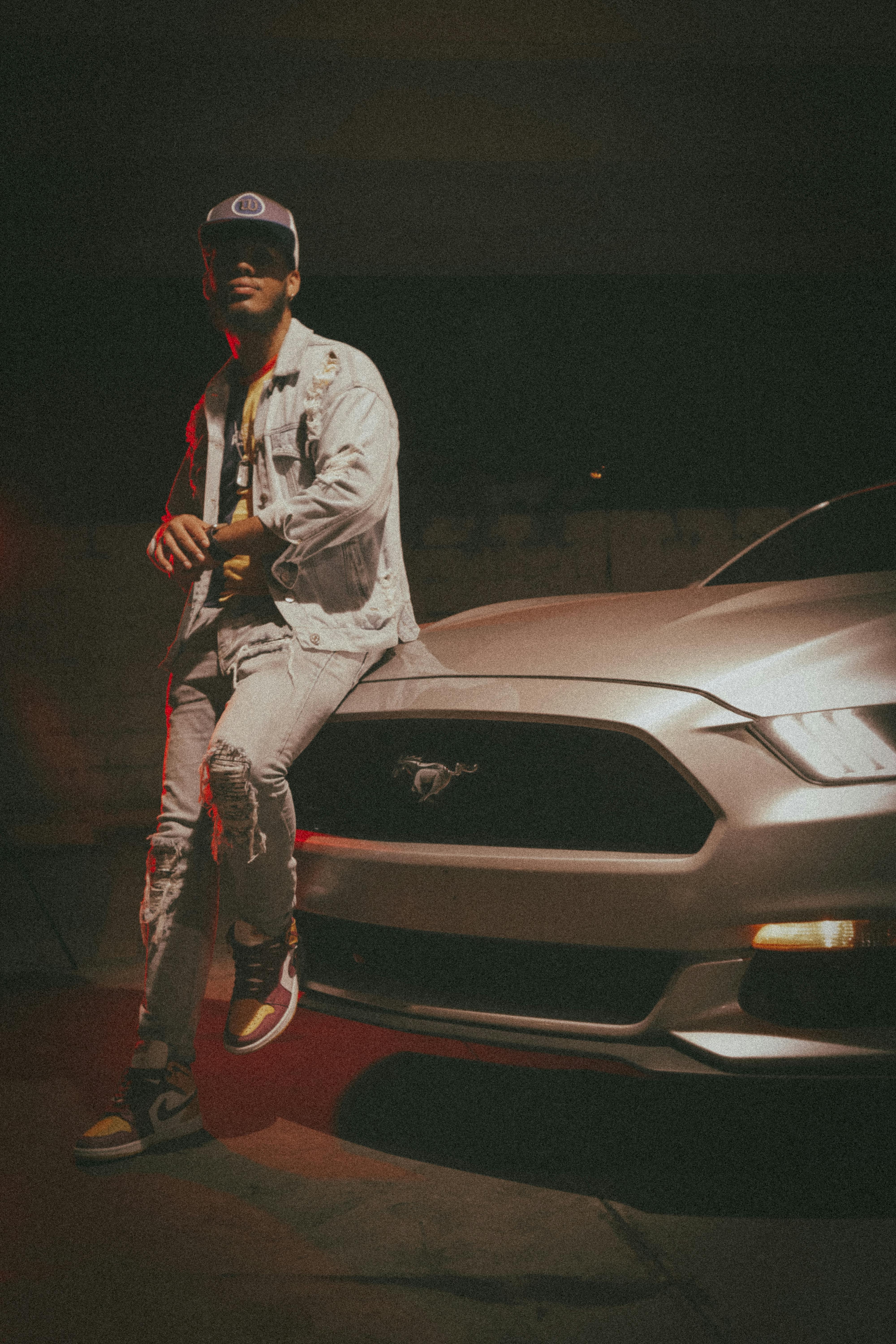 Man in streetwear leaning on a car at night, capturing an urban cool vibe.