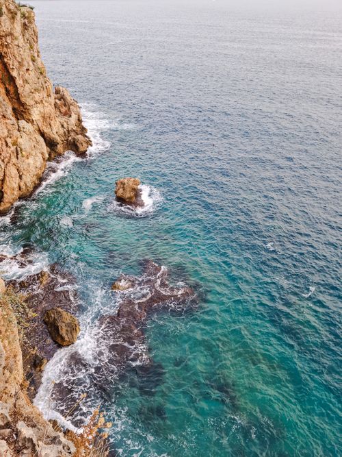 Free Breathtaking view of rugged cliffs beside turquoise sea waves creating a dramatic coastal landscape. Stock Photo