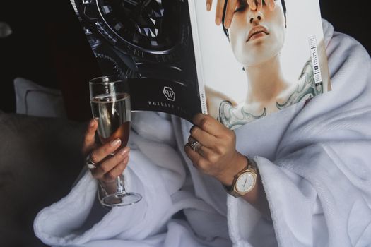 Person in bathrobe enjoying a luxurious moment with a magazine and a glass of wine.