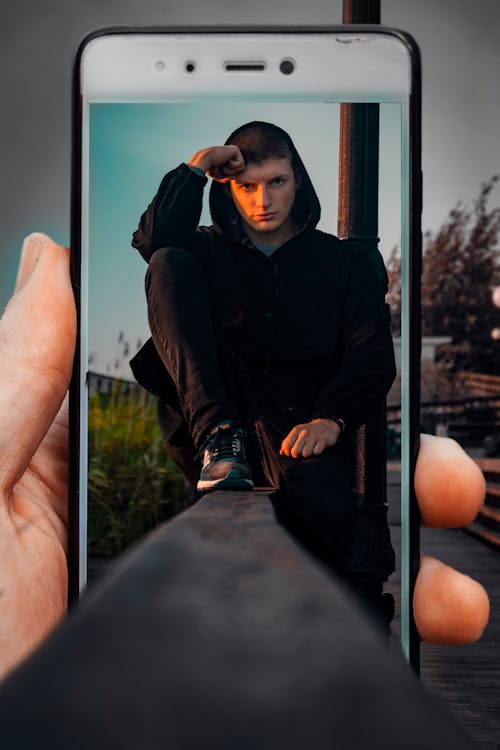 Person Holding Smartphone Displaying Man Sitting On Railing