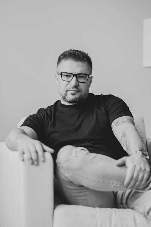 Black and White Photo of a Man Sitting on a Sofa 