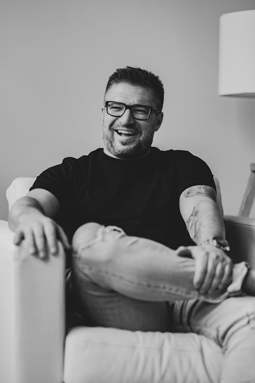 Grayscale Photography of a Happy Man Sitting on a Couch