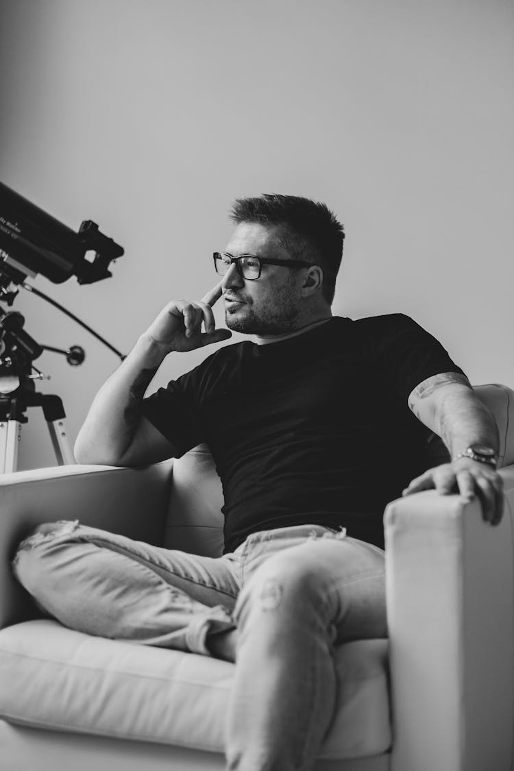 Grayscale Photo Of A Man Sitting On A Sofa