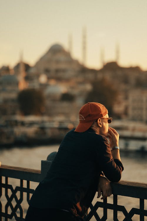 A Man Wearing Cap Leaning on a Guard Rail while Looking Afar