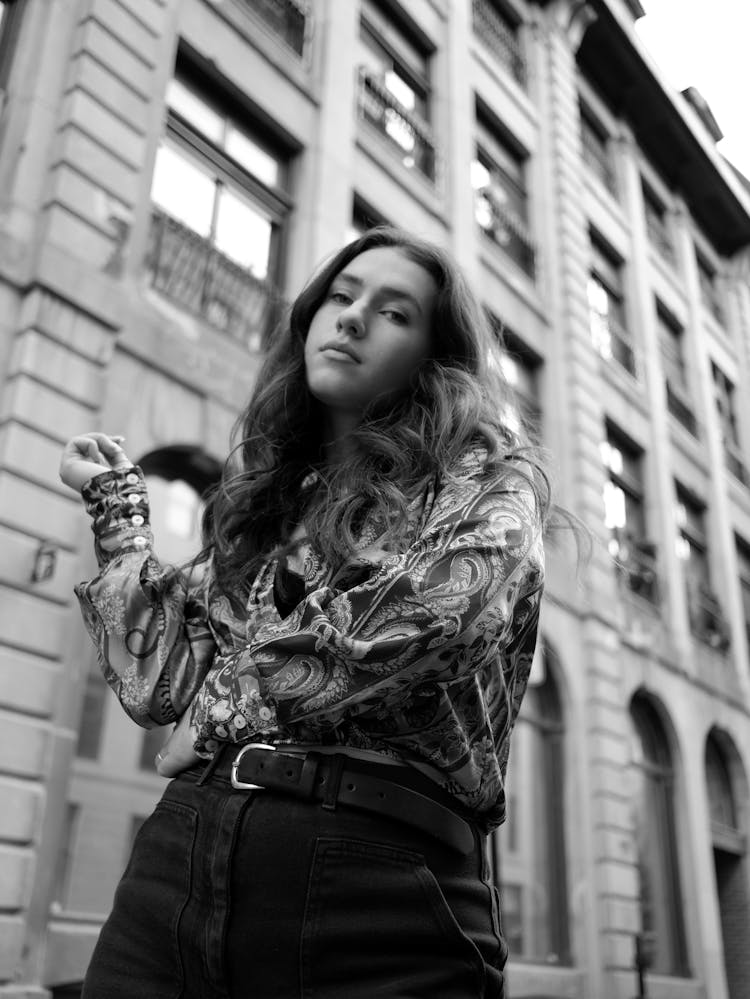 Grayscale Photo Of Low Angle Shot Of Woman Posing Near Building