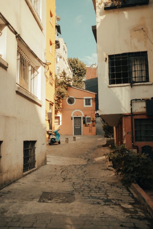 Free A quaint urban alley featuring a vibrant orange building and cobblestone path under a clear sky. Stock Photo
