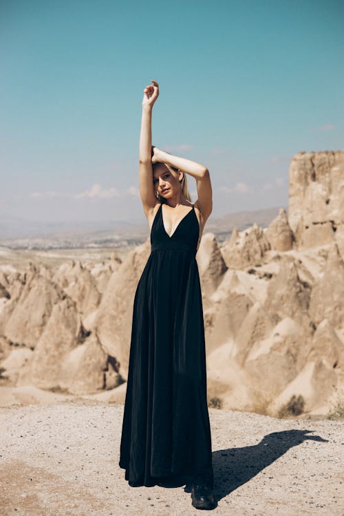 穿著黑色無袖連衣裙的女人站在棕色的沙灘上