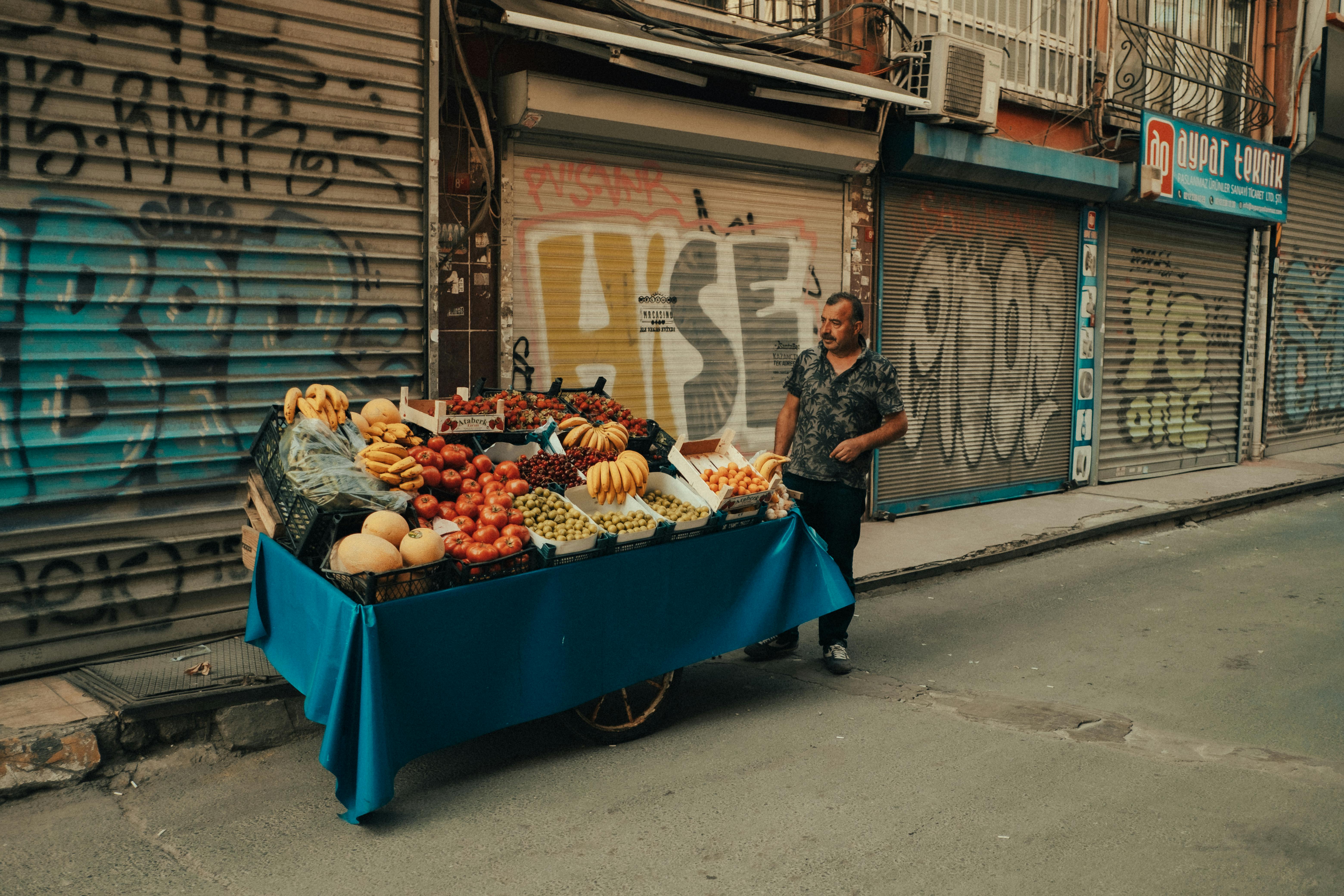Street vendor with a cart full of fresh fruits in a vibrant city alley with graffiti walls.