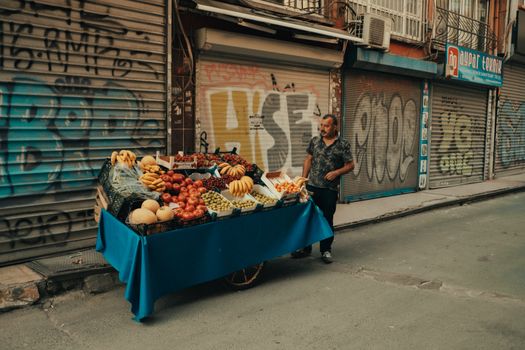 Street vendor with a cart full of fresh fruits in a vibrant city alley with graffiti walls.