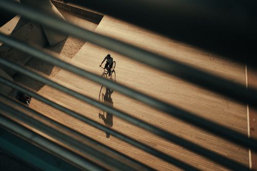 Free A cyclist rides along a wooden path at dusk, captured from an elevated angle, with dramatic shadows and lines. Stock Photo