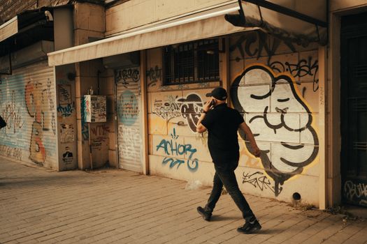 A man in a black shirt walks while talking on the phone past vibrant street art.
