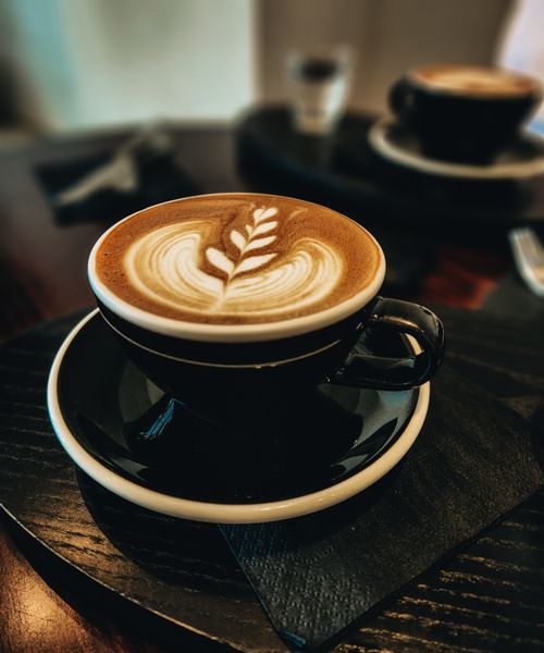 Free Close-up of a cappuccino with delicate latte art in a black ceramic cup, perfect for coffee enthusiasts. Stock Photo