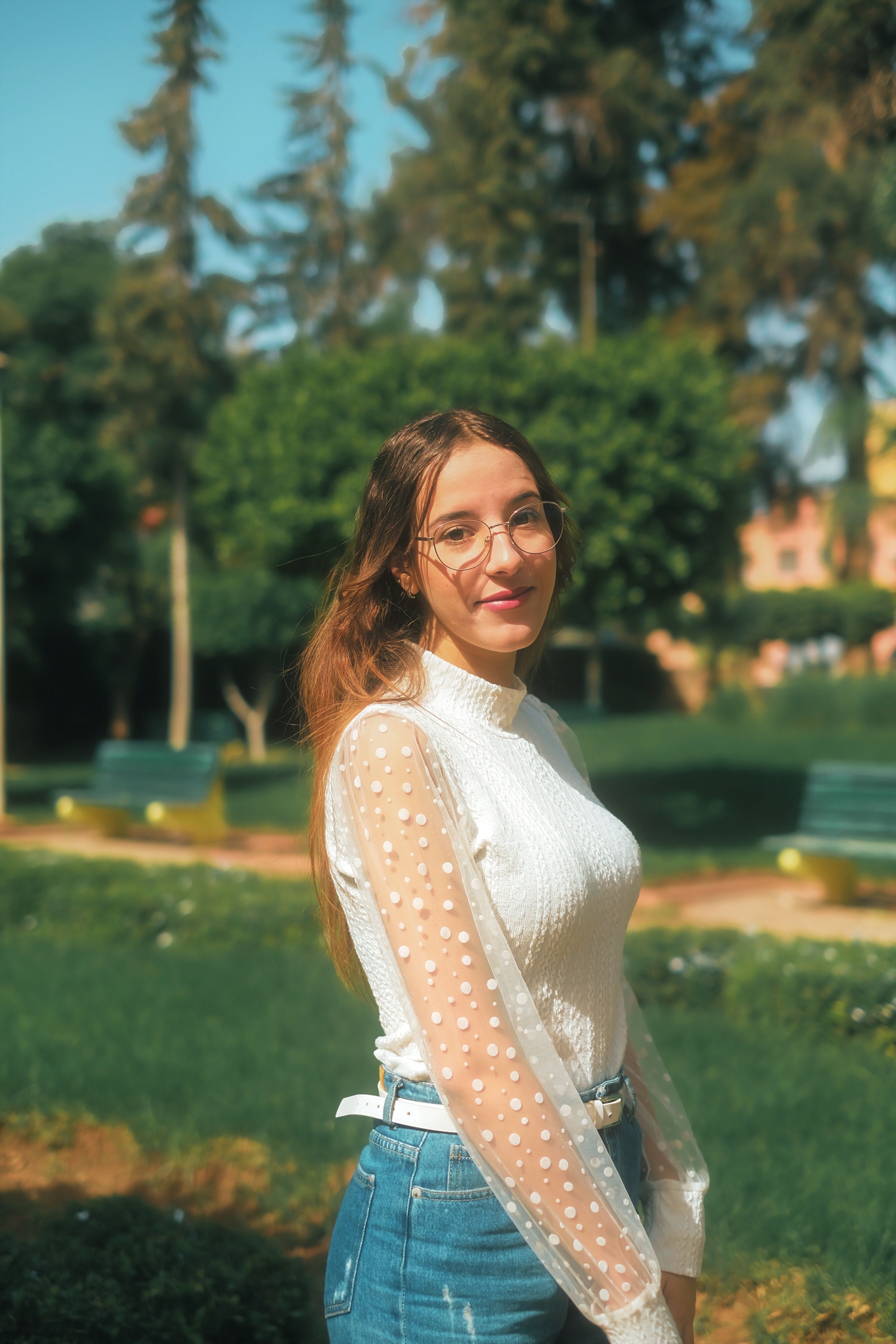 Young woman poses in trendy outfit in a sunny Moroccan park, reflecting fashion and natural beauty.