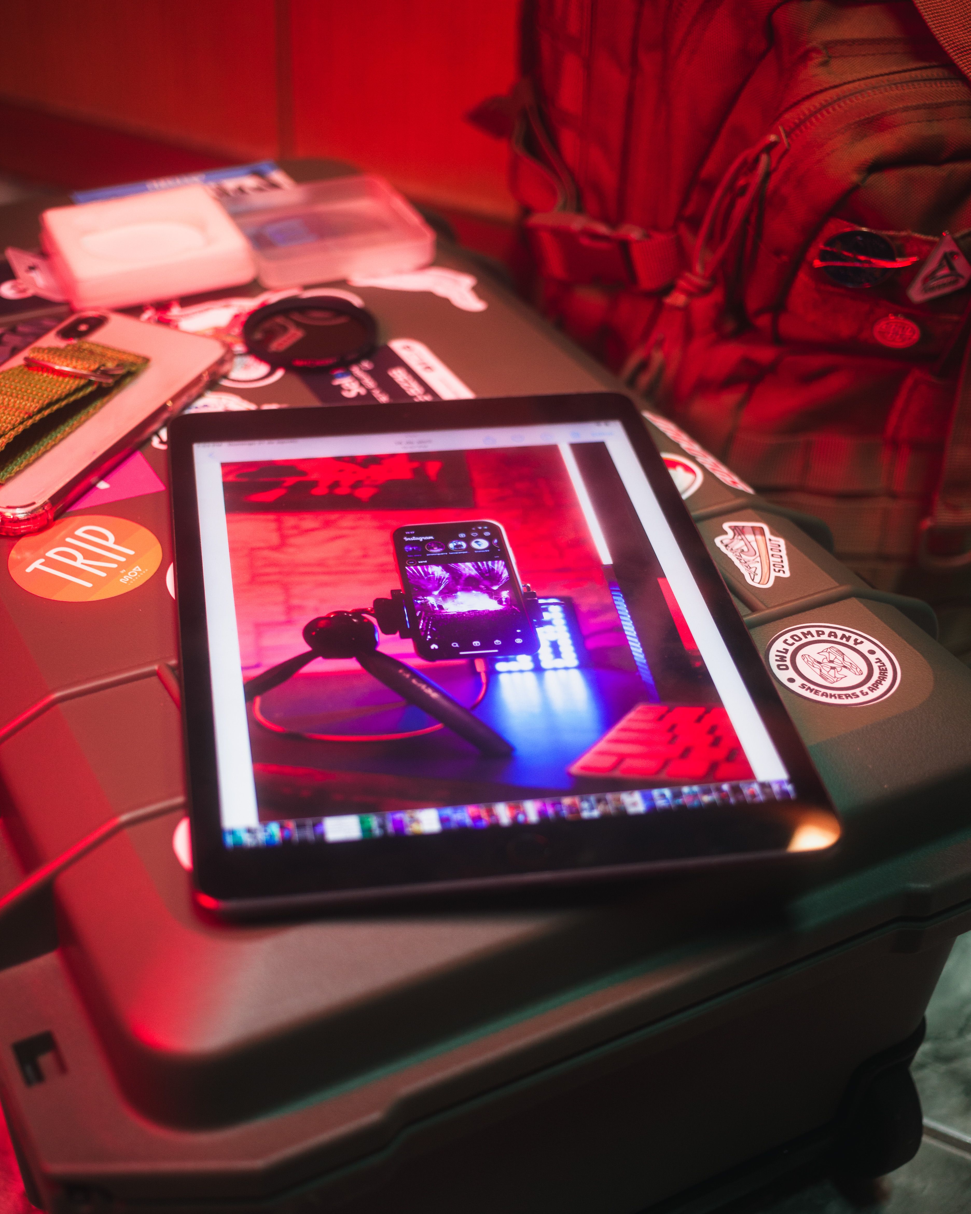 A tablet displaying a smartphone photography setup on a cluttered table with red lighting.