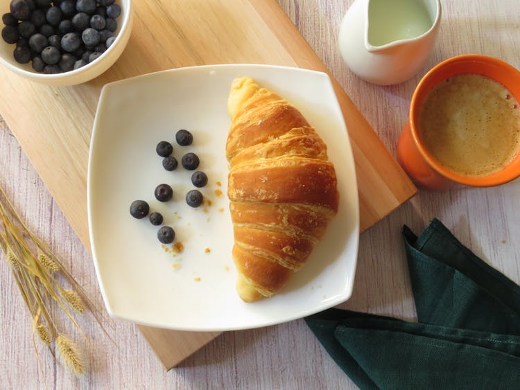 Croissant And Blueberries On Square Ceramic Plate Beside Cup Of Coffee And Milk