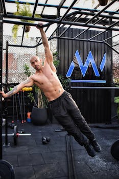 Shirtless man performing pull-up exercise outdoors at a gym, showcasing fitness and strength.