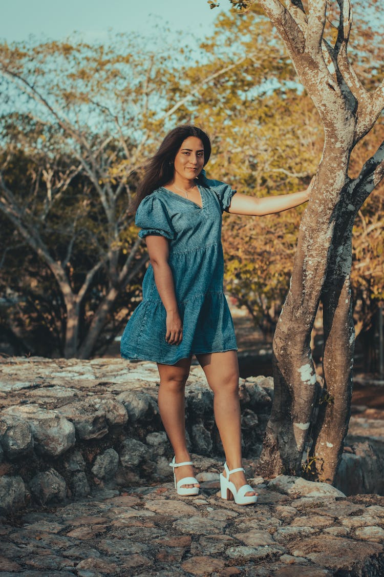 Woman In Denim Dress Standing Beside A Tree