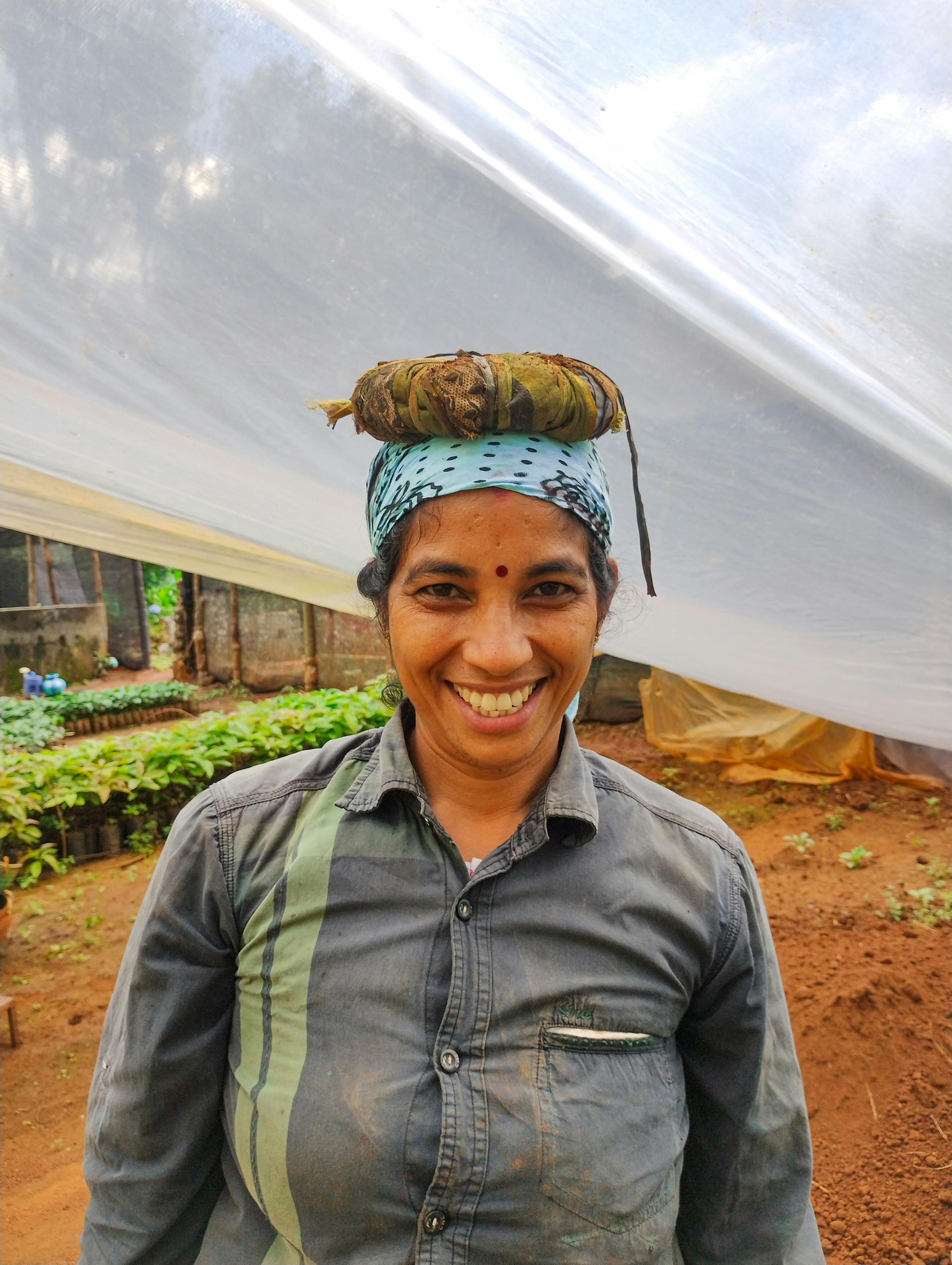 Cheerful South Asian farmer with a headscarf and soil, standing in an Indian greenhouse.