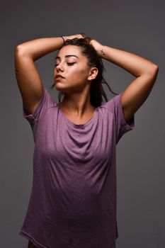 Young woman in a casual t-shirt striking a confident pose with hands up, studio setting.