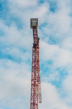 A tall red construction crane stands against a vibrant blue sky with scattered clouds.