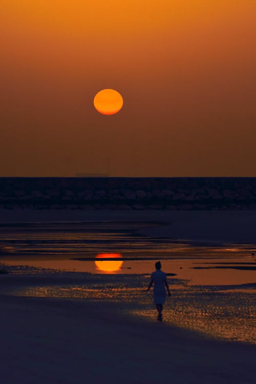 A Person Standing on the Seashore during Sunset