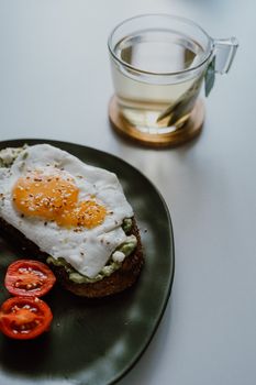 Delicious avocado toast topped with a fried egg and cherry tomatoes, served with a cup of tea.